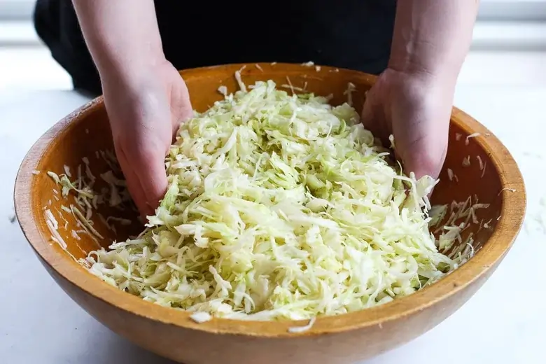 Hands massaging salt into shredded cabbage to create brine for sauerkraut